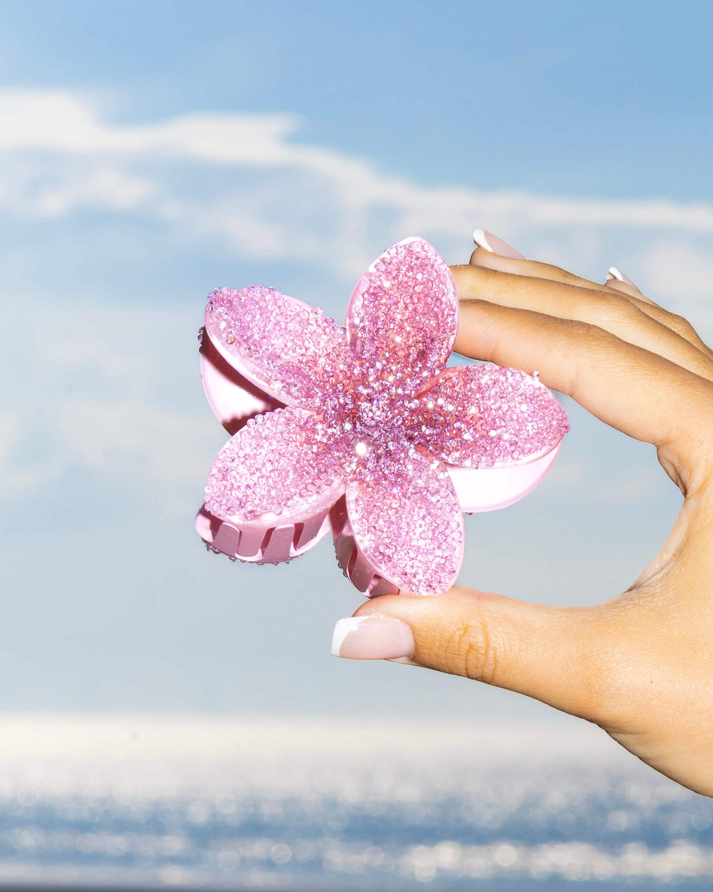 Hand holding a pink diamante flower-shaped clip against the sea