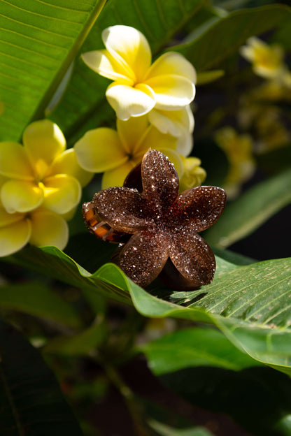Close-up of a brown diamante floral clip surrounded by yellow flowers and green leaves