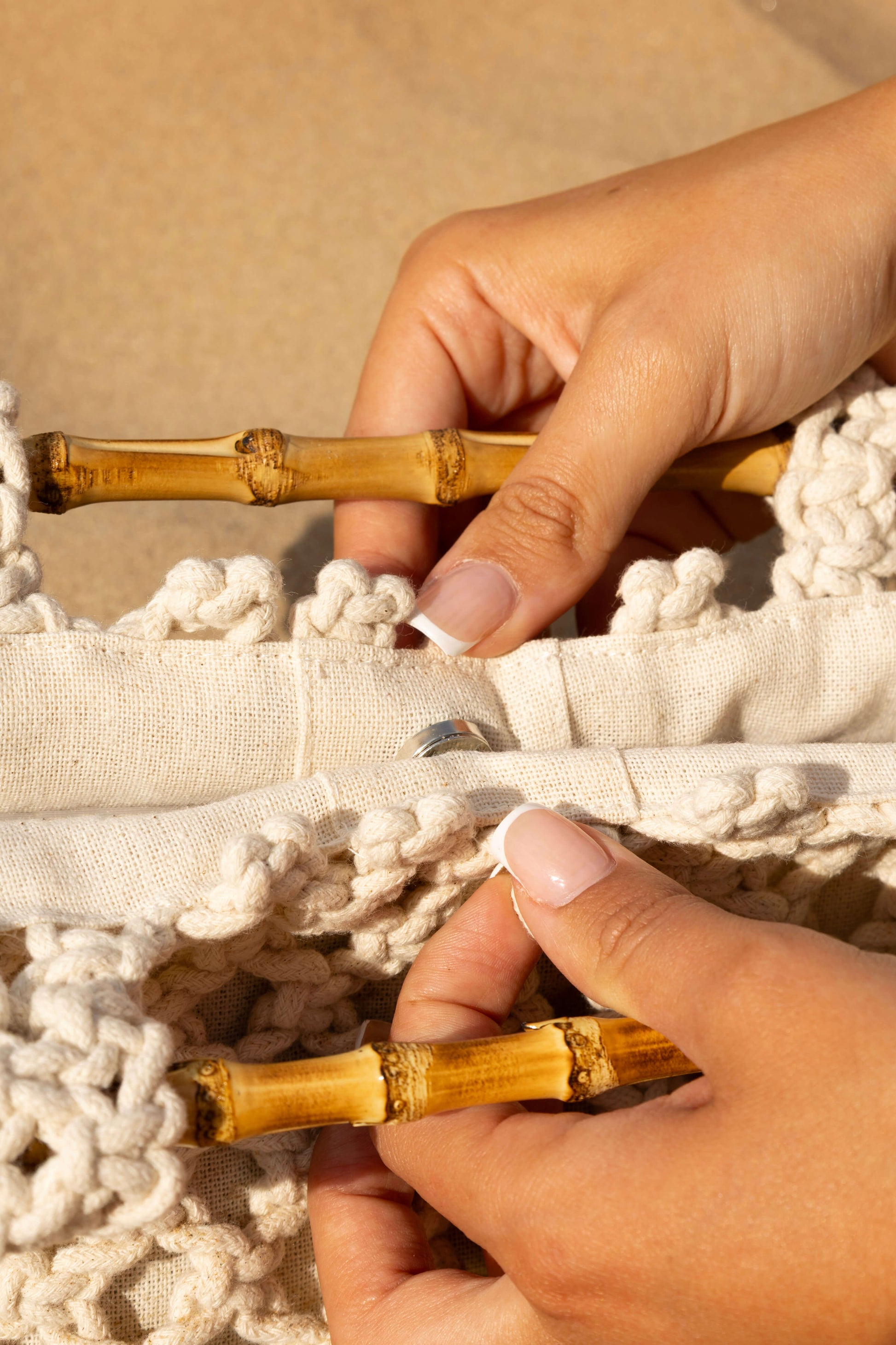 Close-up of hands opening bamboo handles on a cream crochet beach bag