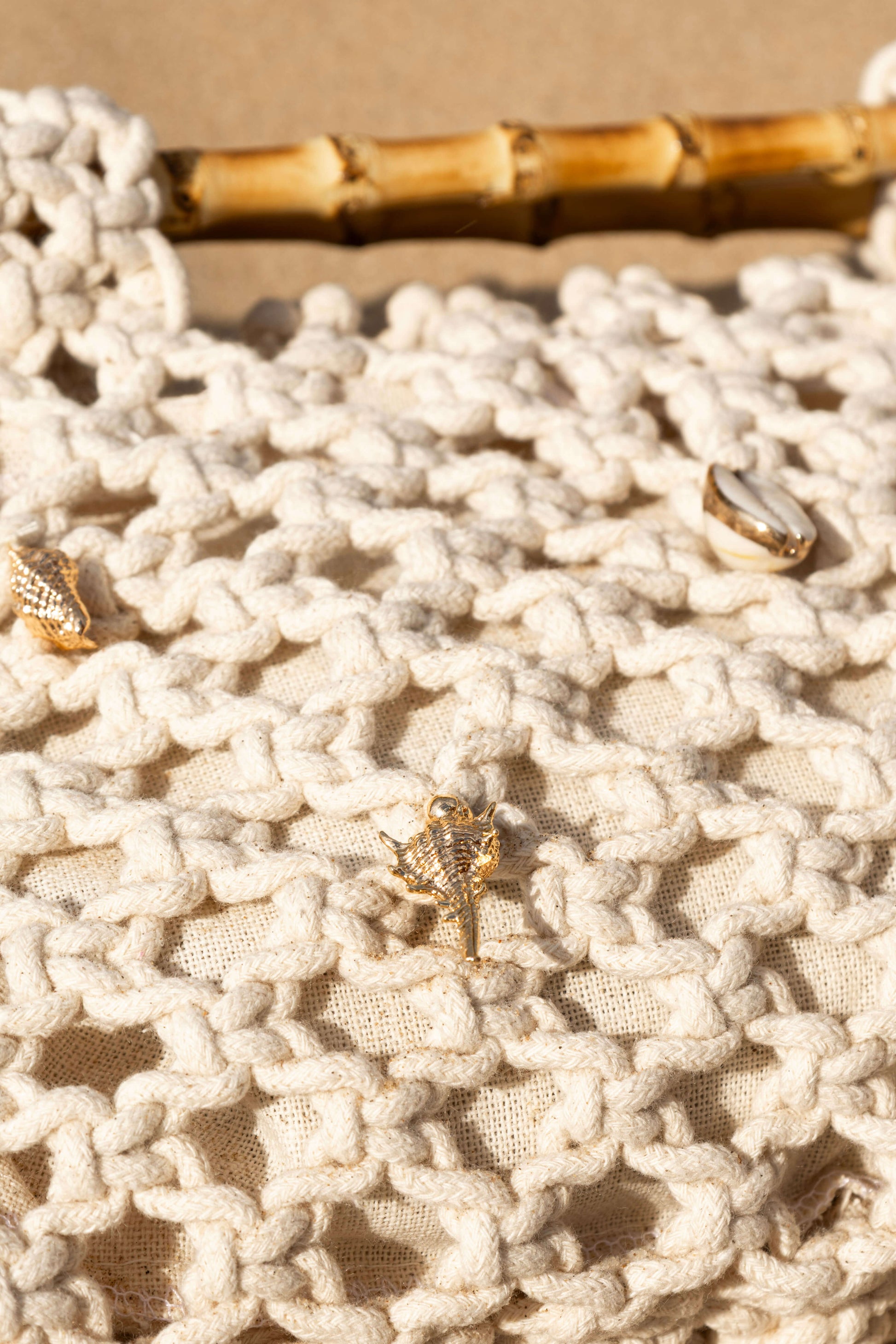 Close up of cream crochet beach bag with gold shell details on sand