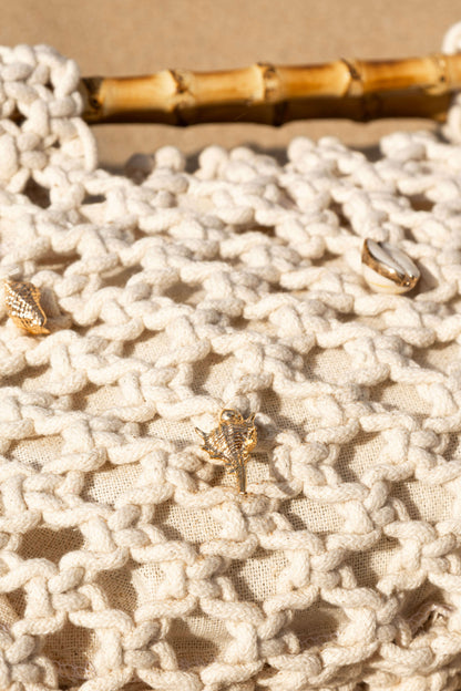 Close up of cream crochet beach bag with gold shell details on sand