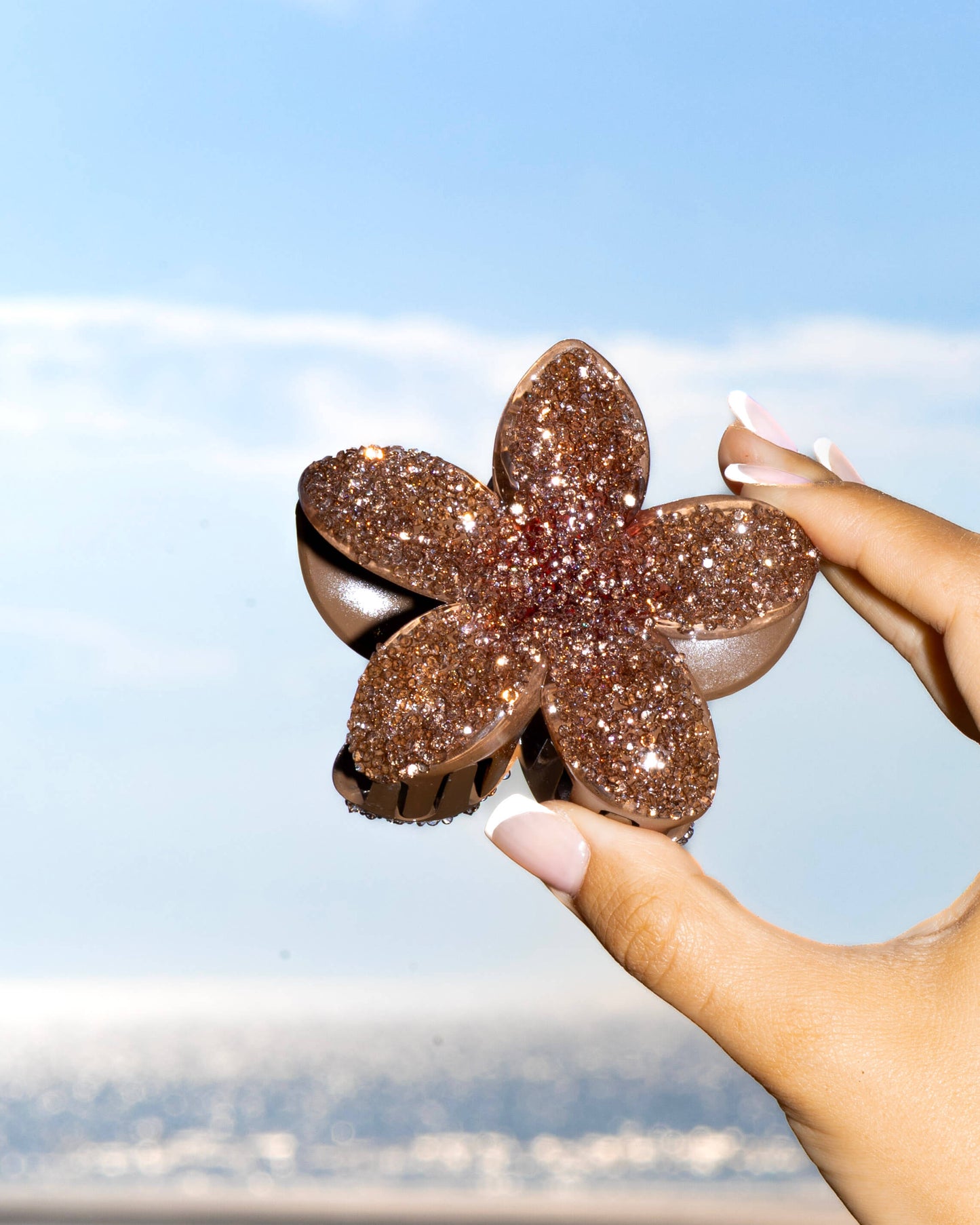 Hand holding a diamante brown flower-shaped hair clip against beach background