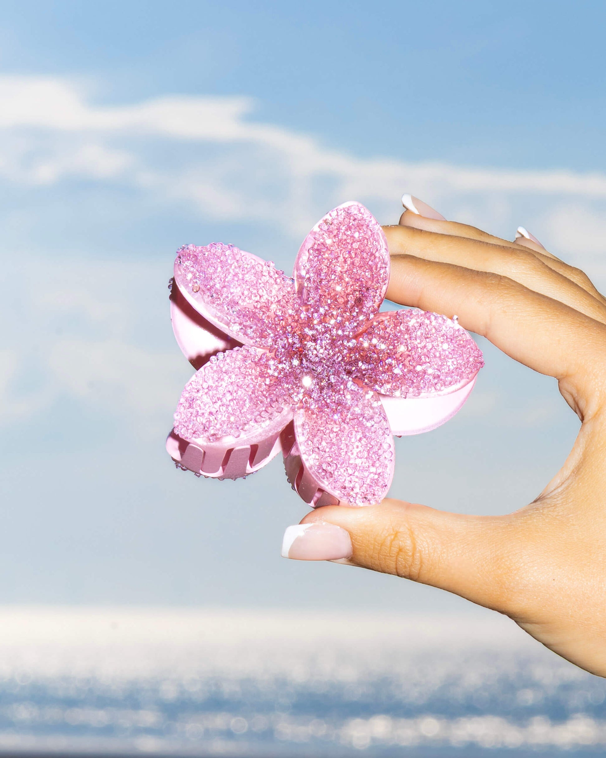 Hand holding a pink diamante flower-shaped clip against the sea