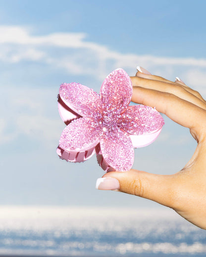 Hand holding a pink diamante flower-shaped clip against the sea