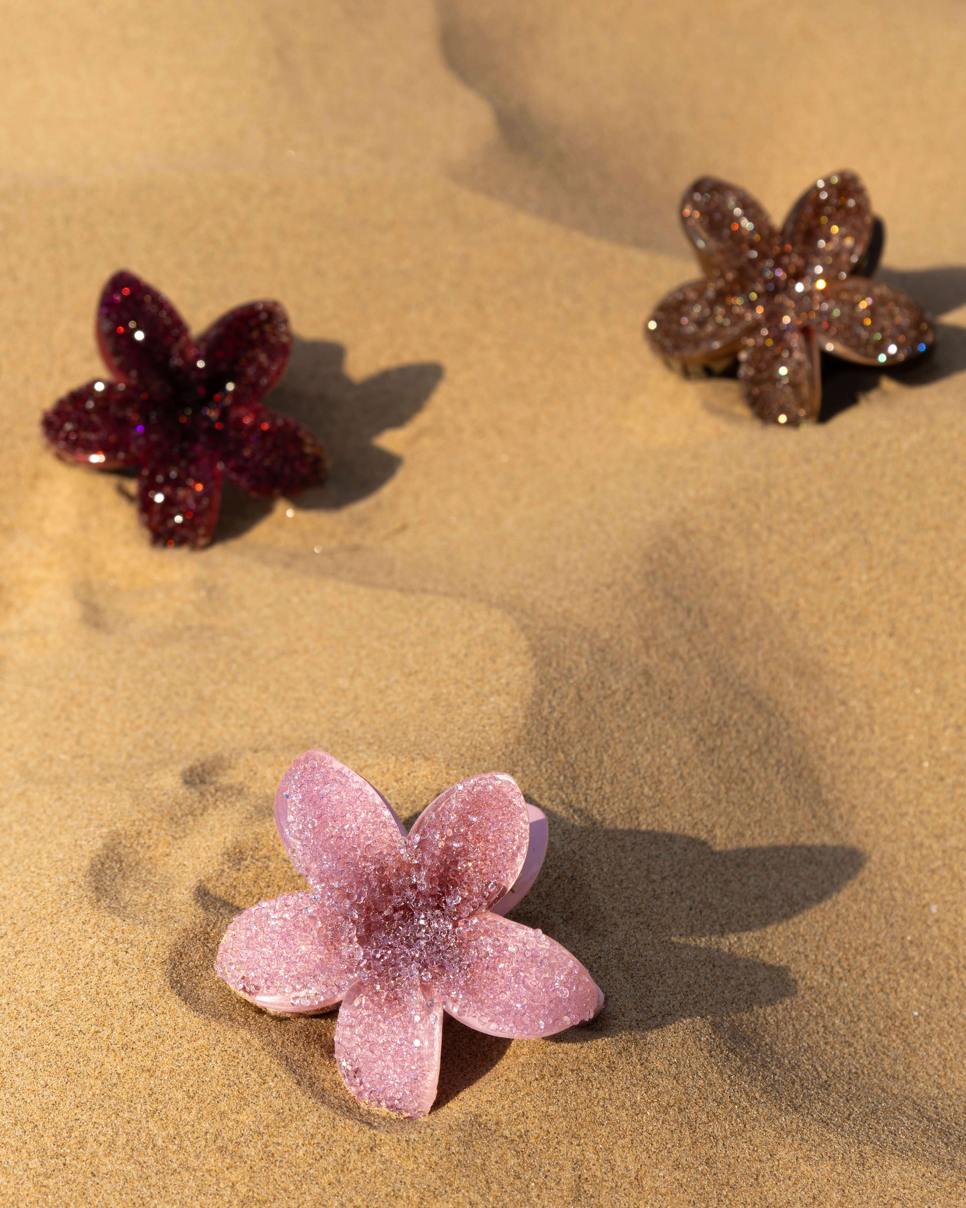 A pink, burgundy and brown diamante floral clip in sand