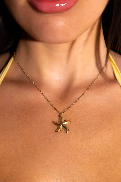 Close-up of a person wearing a gold starfish pendant necklace by opulence